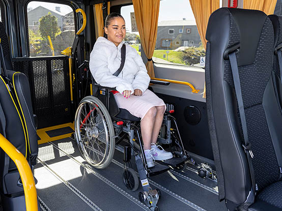 Personne assise dans un fauteuil roulant avec dispositif de retenue des occupants et du fauteuil roulant