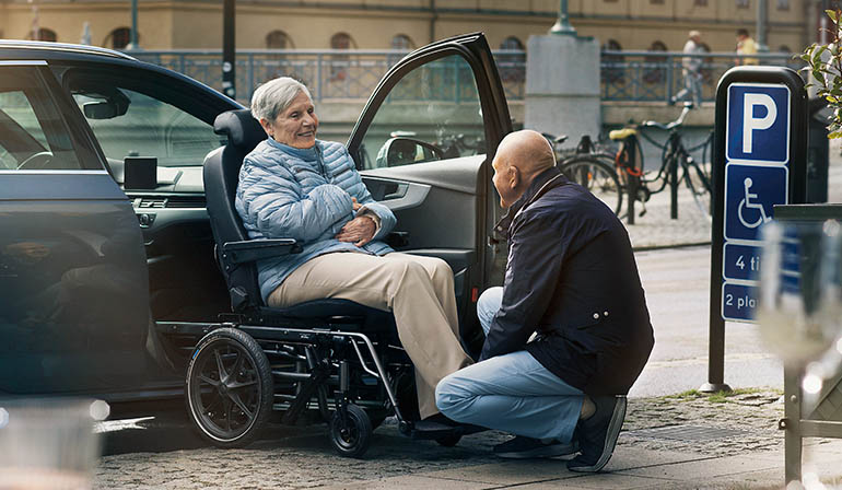 Woman sitting in a Carony is being assisted into the car by a man